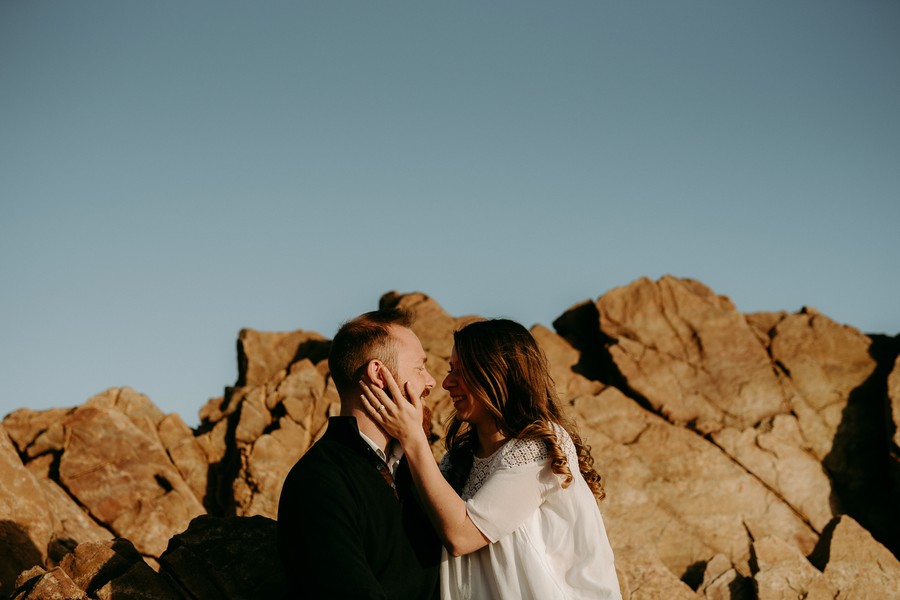 couple engagement se regarde ciel bleu rochers sourire