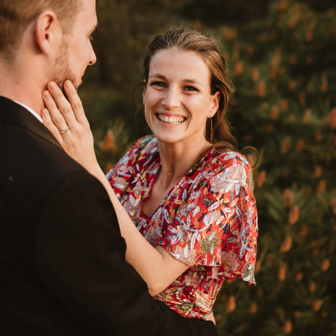 Une jeune femme en robe rouge souriant, elle pose ses mains sur le visage de son conjoint