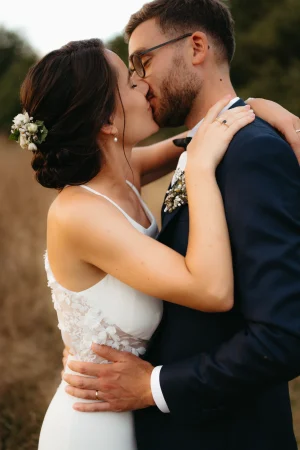 Un couple de mariés en costume bleu et robe de marié s'embrasse pendant leur séance couple le jour de leur mariage