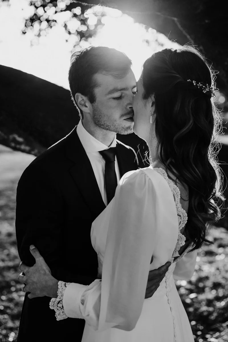 Des mariés s'embrassent le jour de leur mariage avec le soleil en arrière-plan, photo en noir et blanc