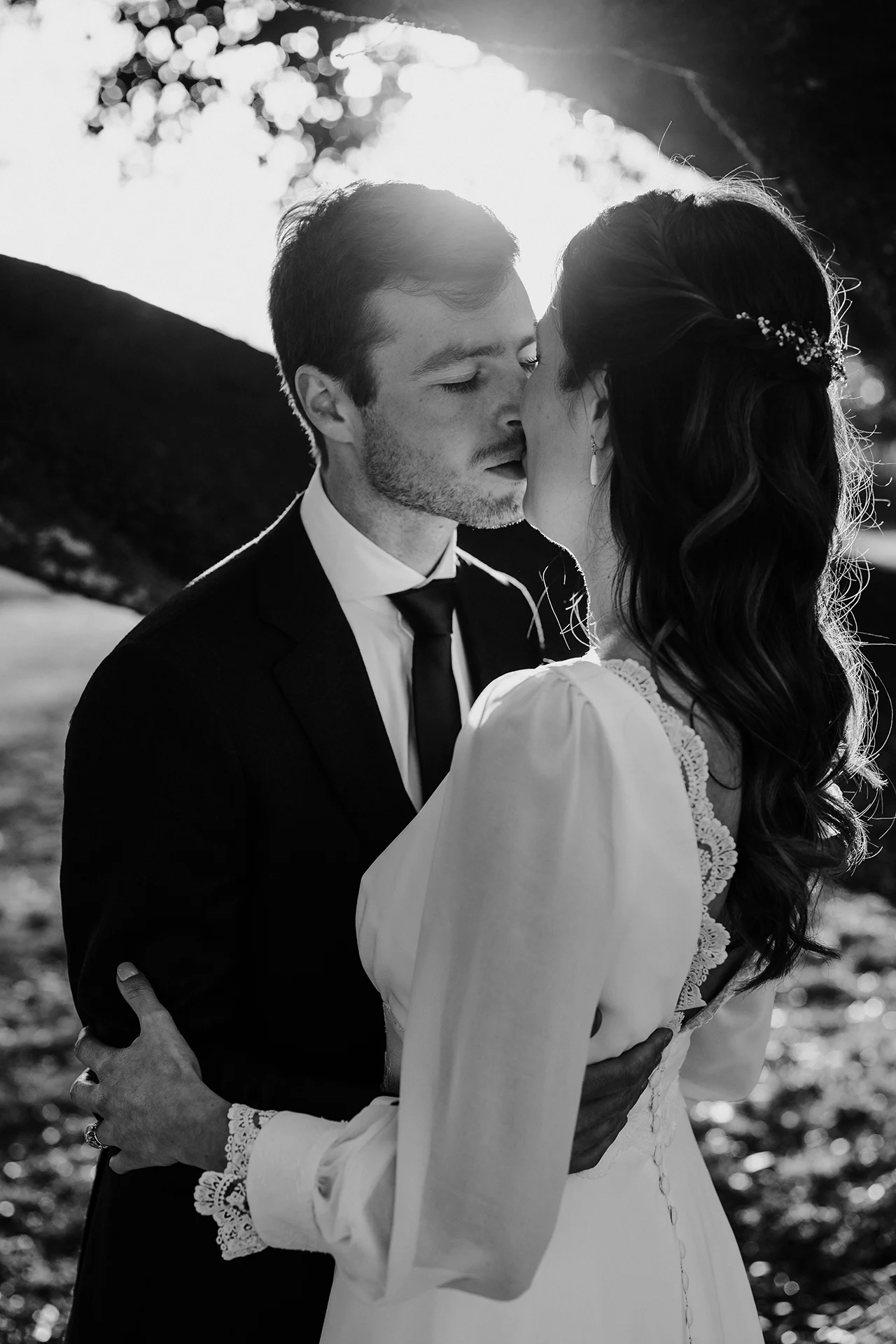 Des mariés s'embrassent le jour de leur mariage avec le soleil en arrière-plan, photo en noir et blanc